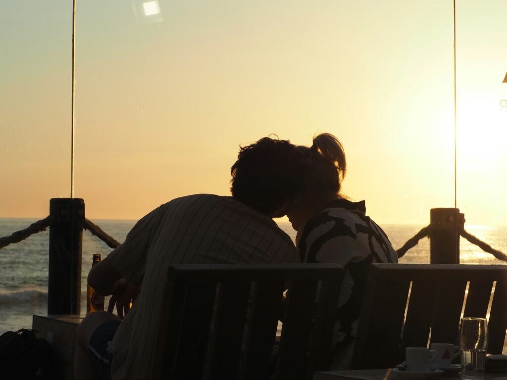 a man and a woman sitting on a bench in front of the ocean